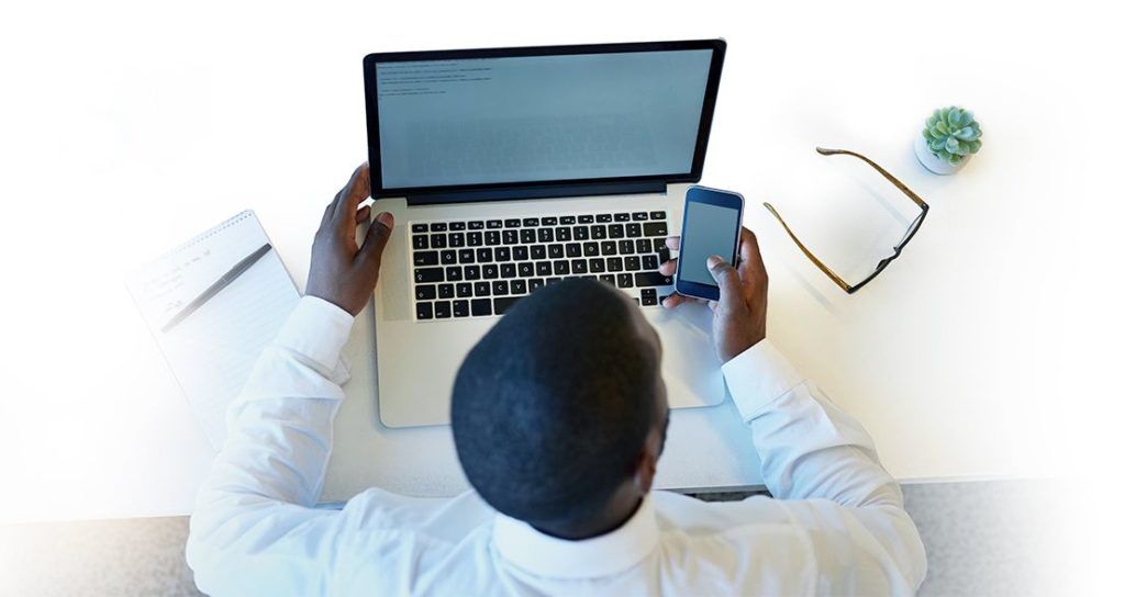 A man sitting in front of his laptop checking his mobile phone