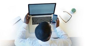 A man sitting in front of his laptop checking his mobile phone