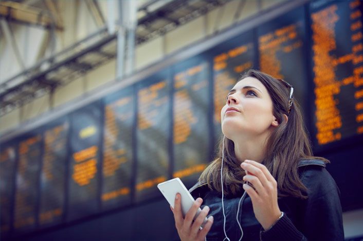 A woman with a mobile phone and headset in front of the flight info screens at an airport